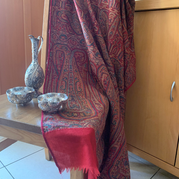 Photo of a red and orange sari with sophisticated pattern and red band around the edges hanging from the back of the chair, while on the seat there are some Indian silver finger bowls